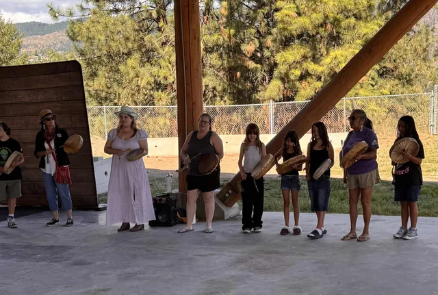 This photograph shows Roxanne Lindley, Syilx (Okanagan) leader from British Columbia, Canada, during a community gathering with women from her Nation. The women are engaged in a traditional drum circle, using Indigenous hand drums as part of a cultural ceremony and practice. Indigenous community platforms and networks in Canada
