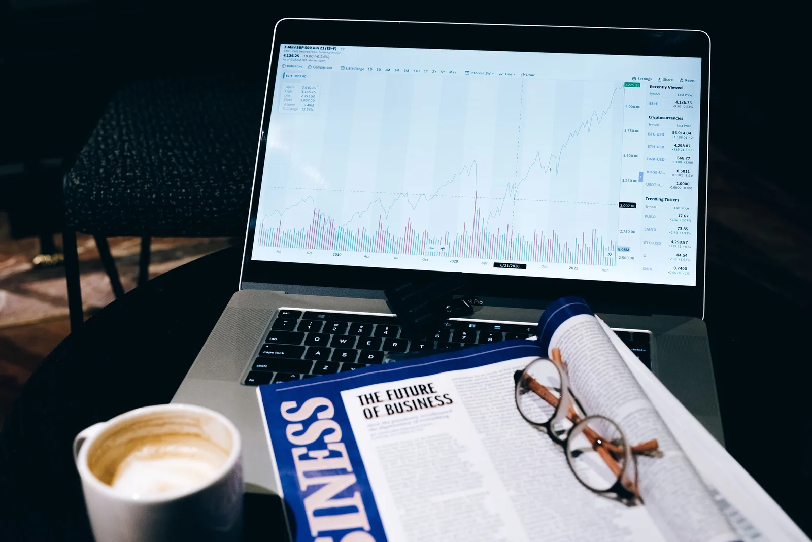 A modern business workspace featuring a laptop showing stock data next to a business magazine and coffee. Reading major social networks data without fooling yourself
